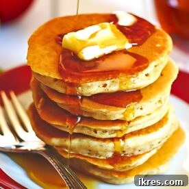 A stack of fluffy apple cinnamon pancakes drizzled with maple syrup and topped with butter slices.
