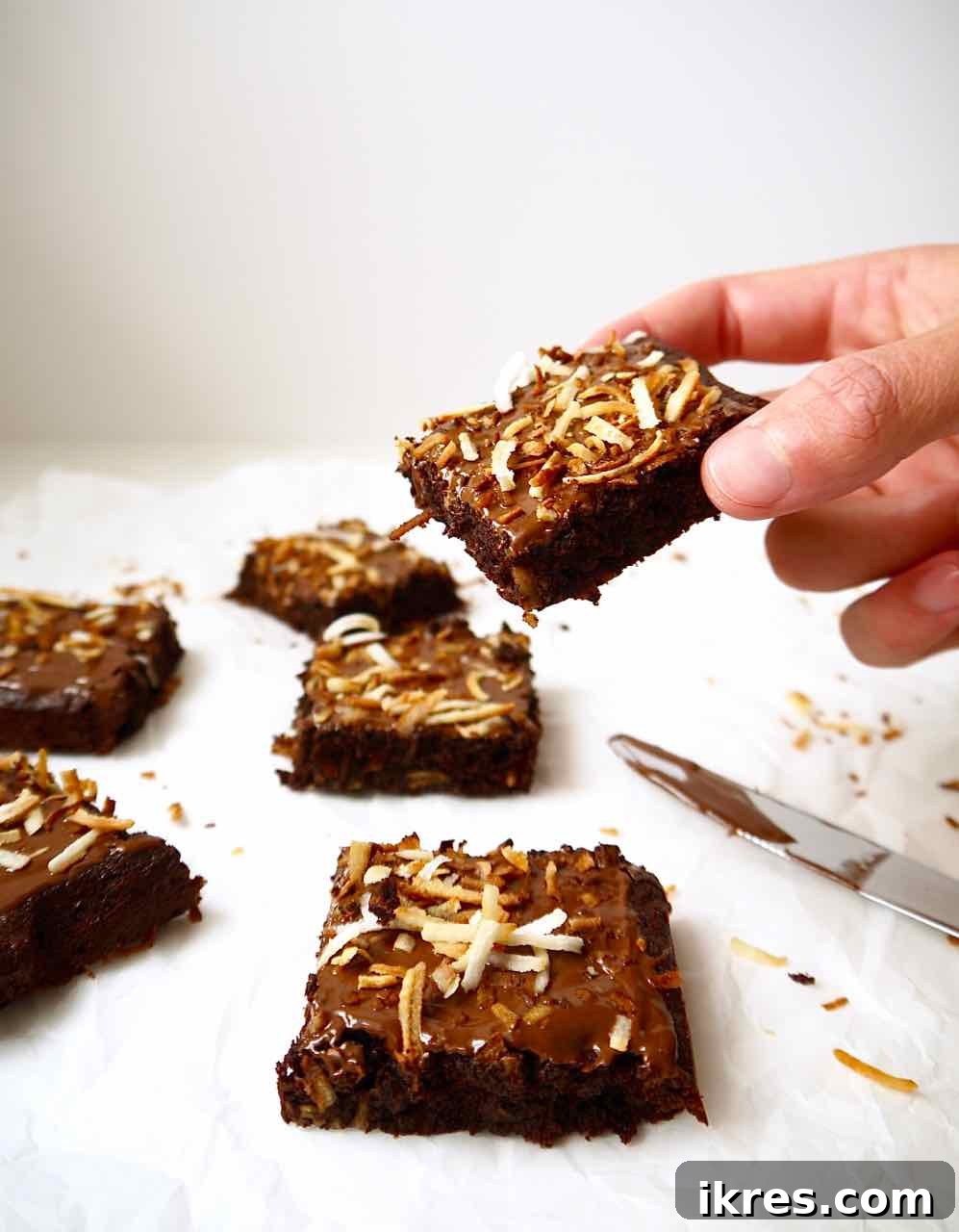 Gluten-Free Toasted Coconut Cloud Brownies 10 A hand reaching for a delicious coconut chocolate brownie, tempting to take a bite.