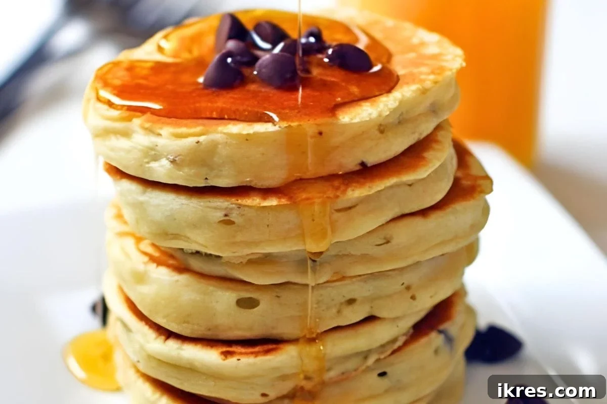 A towering stack of fluffy chocolate chip pancakes, generously drizzled with golden maple syrup and topped with a pat of melting butter, ready for a cozy Christmas breakfast.
