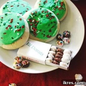 Elf Donuts on a white plate with cookies, decorated with green and red frosting and sprinkles.