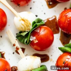 Caprese Skewers with grape tomatoes, mozzarella, and basil, drizzled with balsamic glaze, arranged festively.