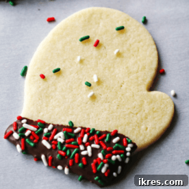 A festive mitten-shaped sugar cookie decorated with white icing and sprinkles, ready for holiday celebrations.