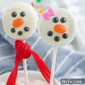 Adorable Snowman Oreo Pops dipped in white chocolate and decorated with mini chocolate chips and an orange nose.