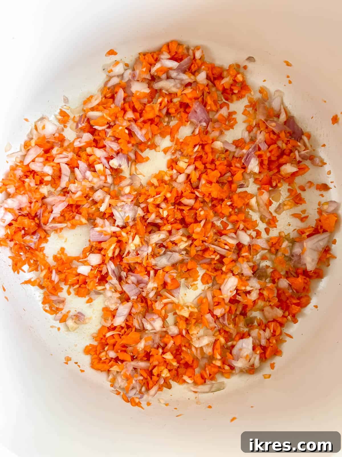 Minced carrot, onion, and garlic gently cooking in olive oil in a large pan, forming the aromatic base for the bolognese.