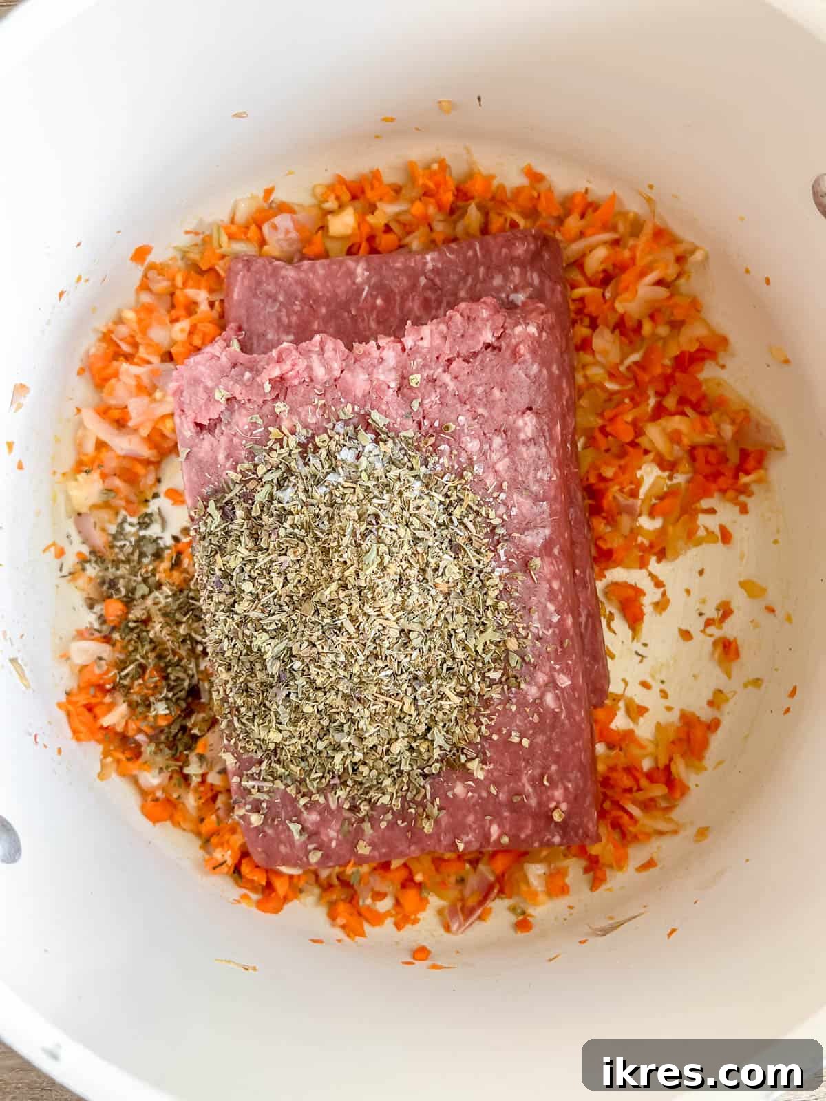 Ground bison, seasoned with Italian herbs, added directly on top of the sautéed carrots, onions, and garlic in the pan.
