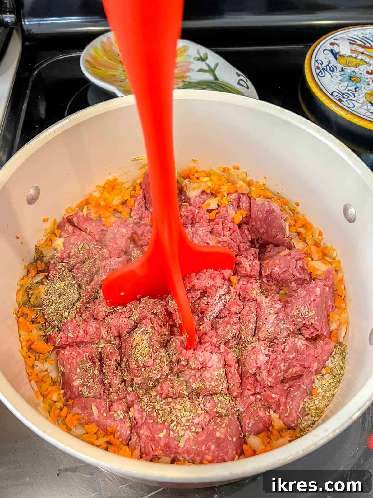 A meat masher being used to break up ground bison into finer pieces as it cooks in the pan.