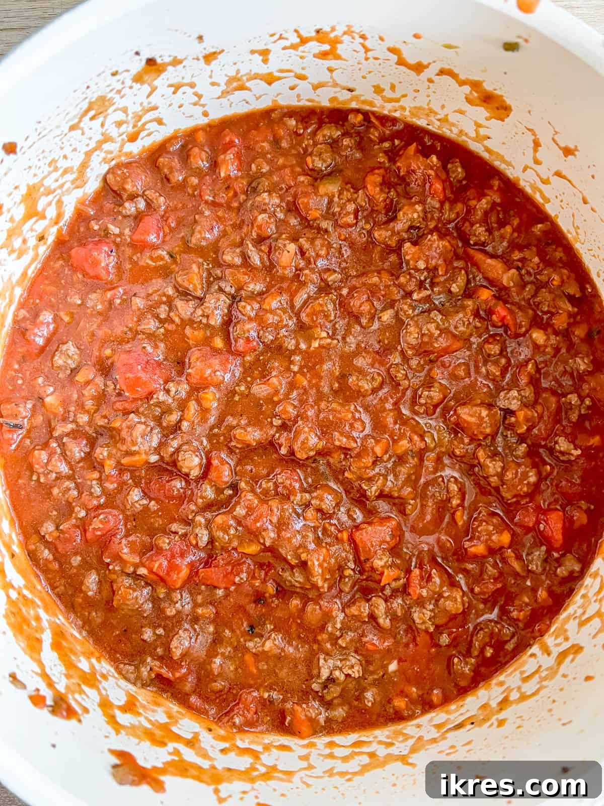 Strained and crushed tomatoes, along with water, being poured into the pan with the bison and tomato paste, ready for simmering.