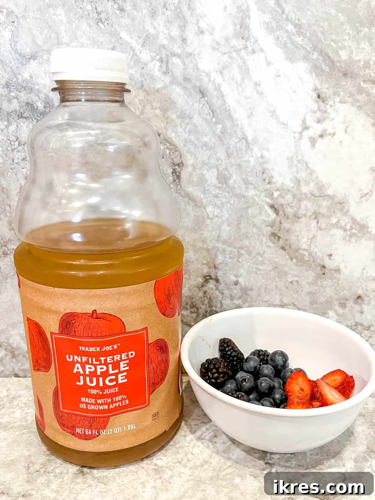 Fresh apple juice and a vibrant mix of berries laid out as ingredients for homemade popsicles.
