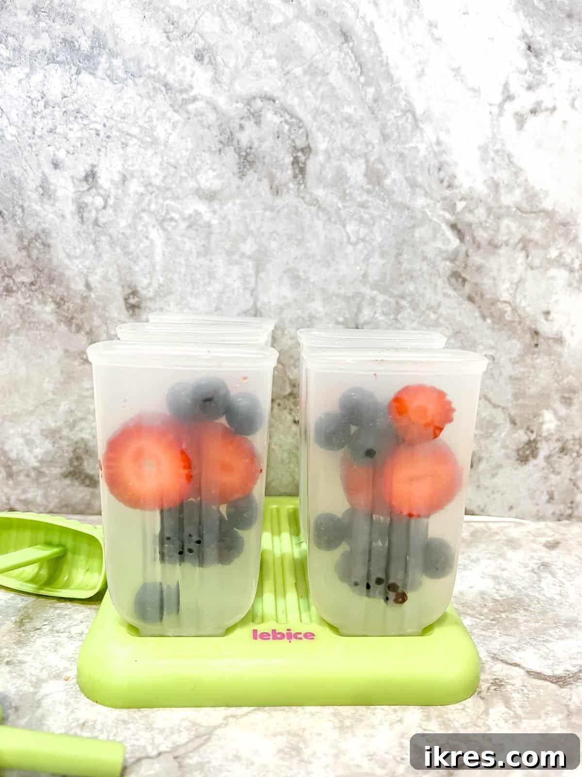Mixed berries being placed into individual popsicle molds.