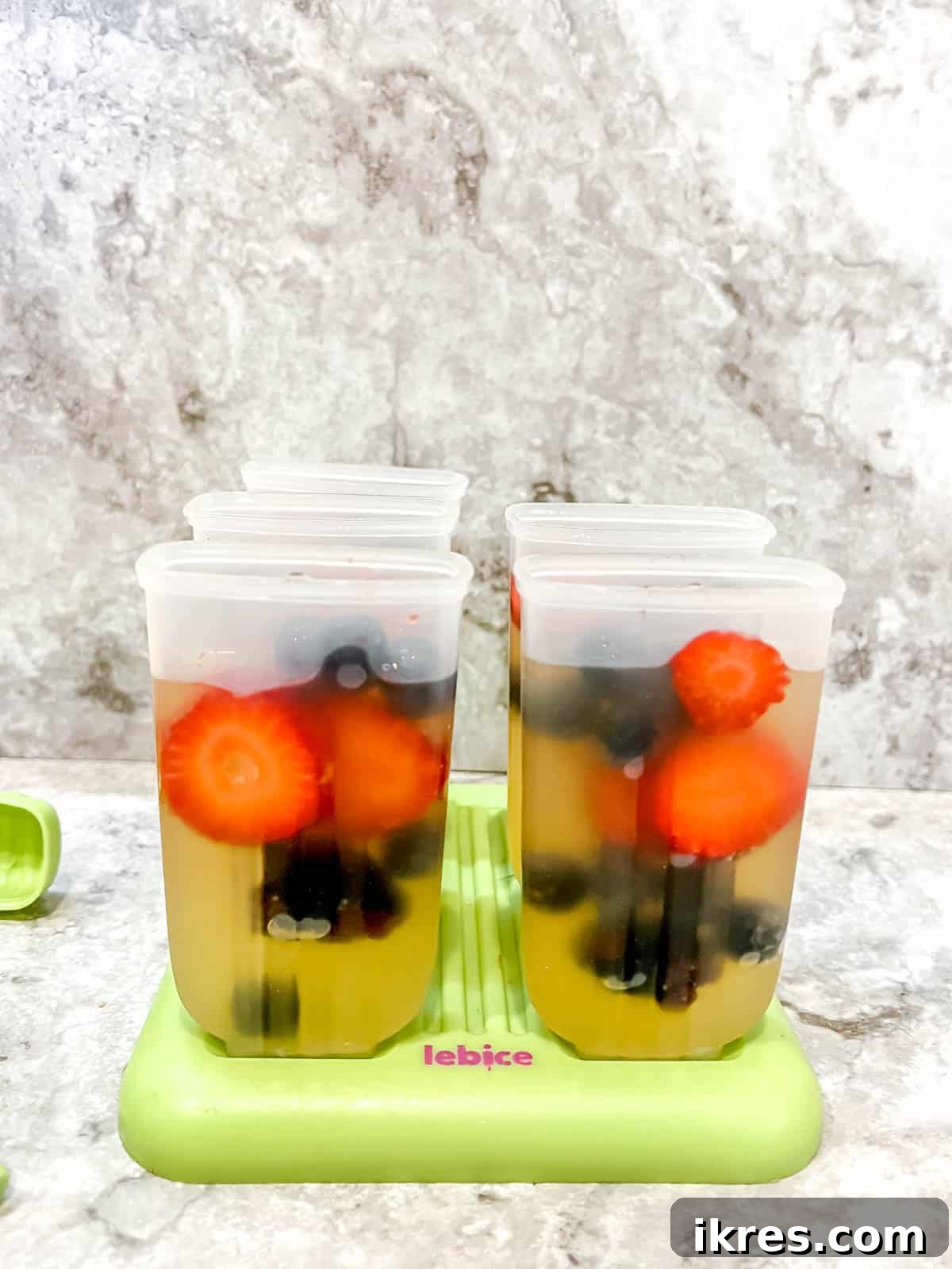 Apple juice being poured over berries into popsicle molds.