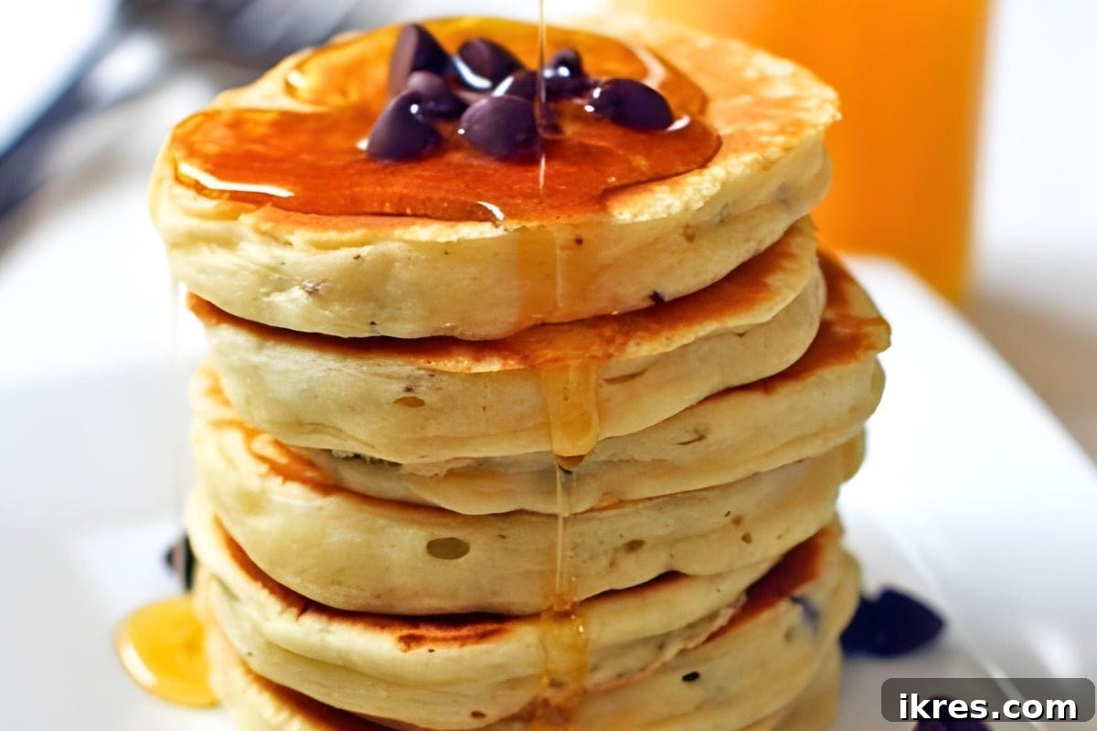 Ultimate Brunch Piled High Pancakes Waffles and Delicious Sauces 2 A stack of fluffy chocolate chip pancakes with maple syrup drizzled on them, creating a mouth-watering breakfast scene.