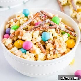 Bunny Bait, a sweet and salty spring snack mix featuring cereal coated in white chocolate, tossed with pastel candies, and dusted with powdered sugar, perfect for Easter celebrations.
