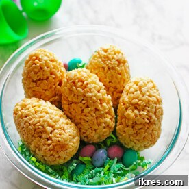 Easter eggs crafted from Rice Krispie treats, filled with colorful M&M's, and artfully arranged in a clear bowl with green Easter grass and additional candies, creating a festive and hidden treat display.