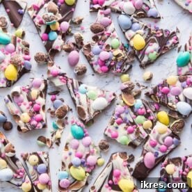 A vibrant Easter candy bark featuring swirls of melted chocolate and pastel candy melts, generously sprinkled with colorful chocolate eggs, festive sprinkles, and crushed cookies for a fun break-apart treat.