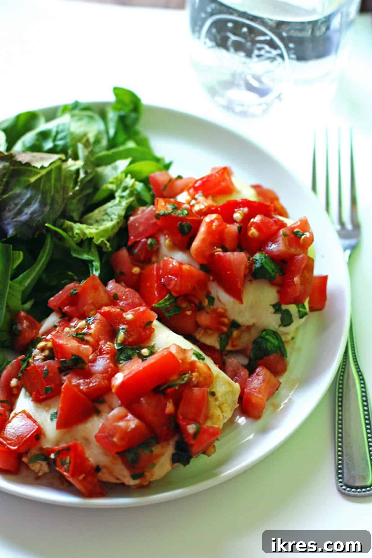 A beautifully plated grilled bruschetta chicken with melted mozzarella, diced tomatoes, and fresh basil, accompanied by a vibrant side salad.