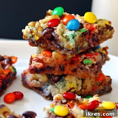 Wondrous Seven-Layer Magic Bars 7 Gooey magic cookie bars with nuts, coconut, chocolate chips, and mini m and ms stacked on a white plate with a glass of milk.