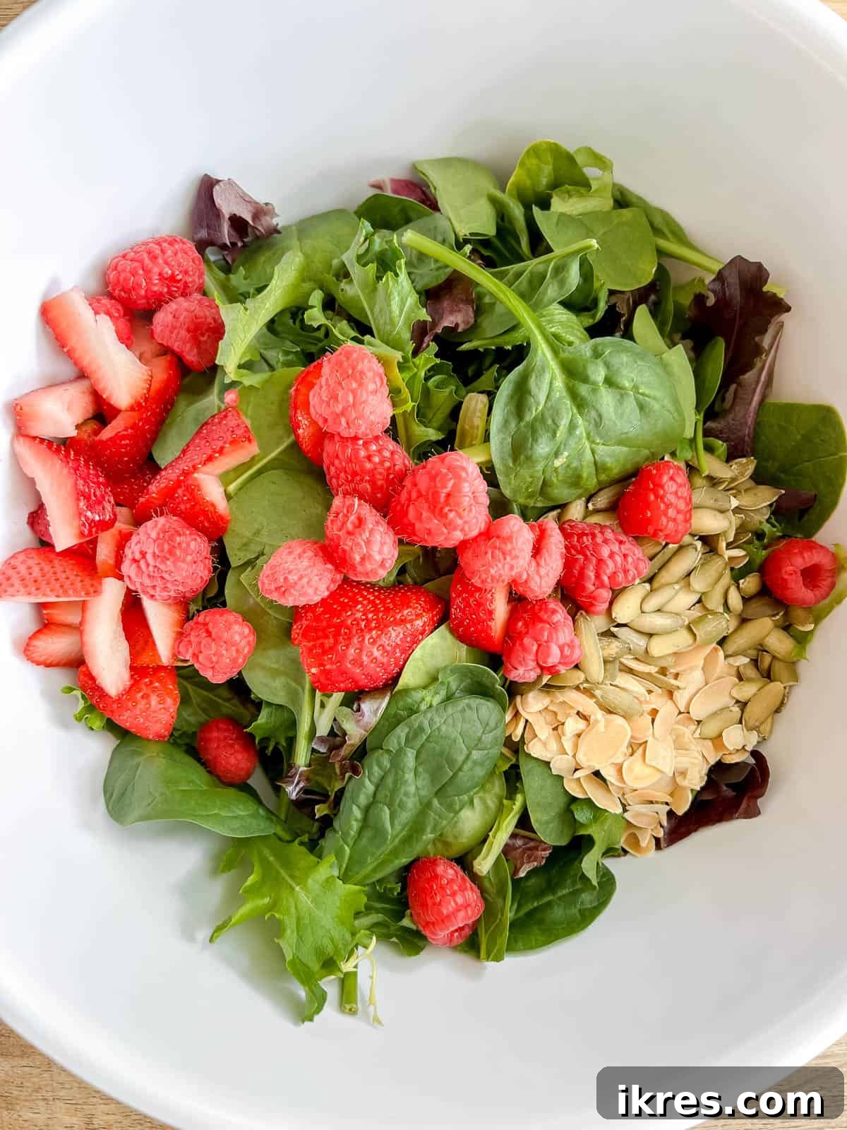 Vibrant Berry and Fig Salad with Creamy Chevre and Vanilla Vinaigrette 5 A large mixing bowl containing a colorful array of mixed greens, fresh strawberries, raspberries, sliced almonds, and pumpkin seeds, awaiting the dressing.