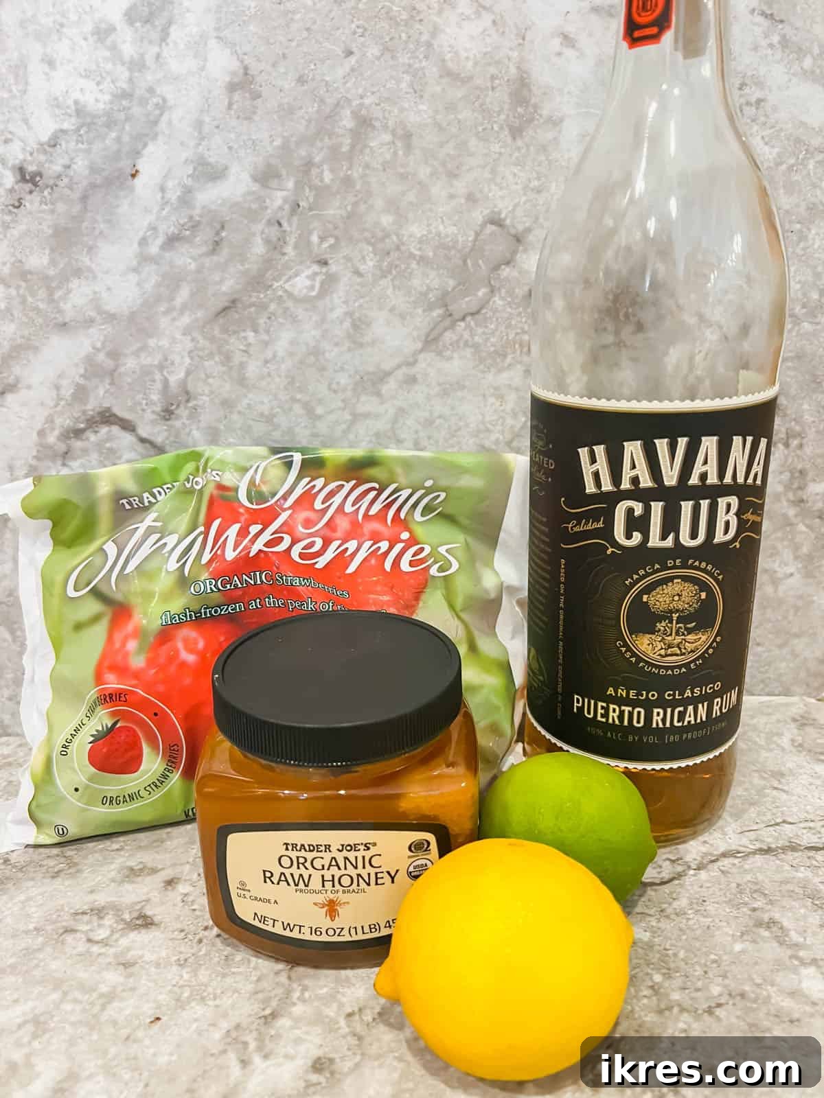 Ingredients needed to make a skinny strawberry daiquiri, including frozen strawberries, citrus fruits, and a bottle of rum.