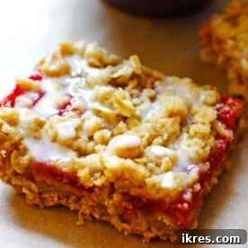 A glazed strawberry rhubarb crumble bar on a tray covered in brown parchment paper.