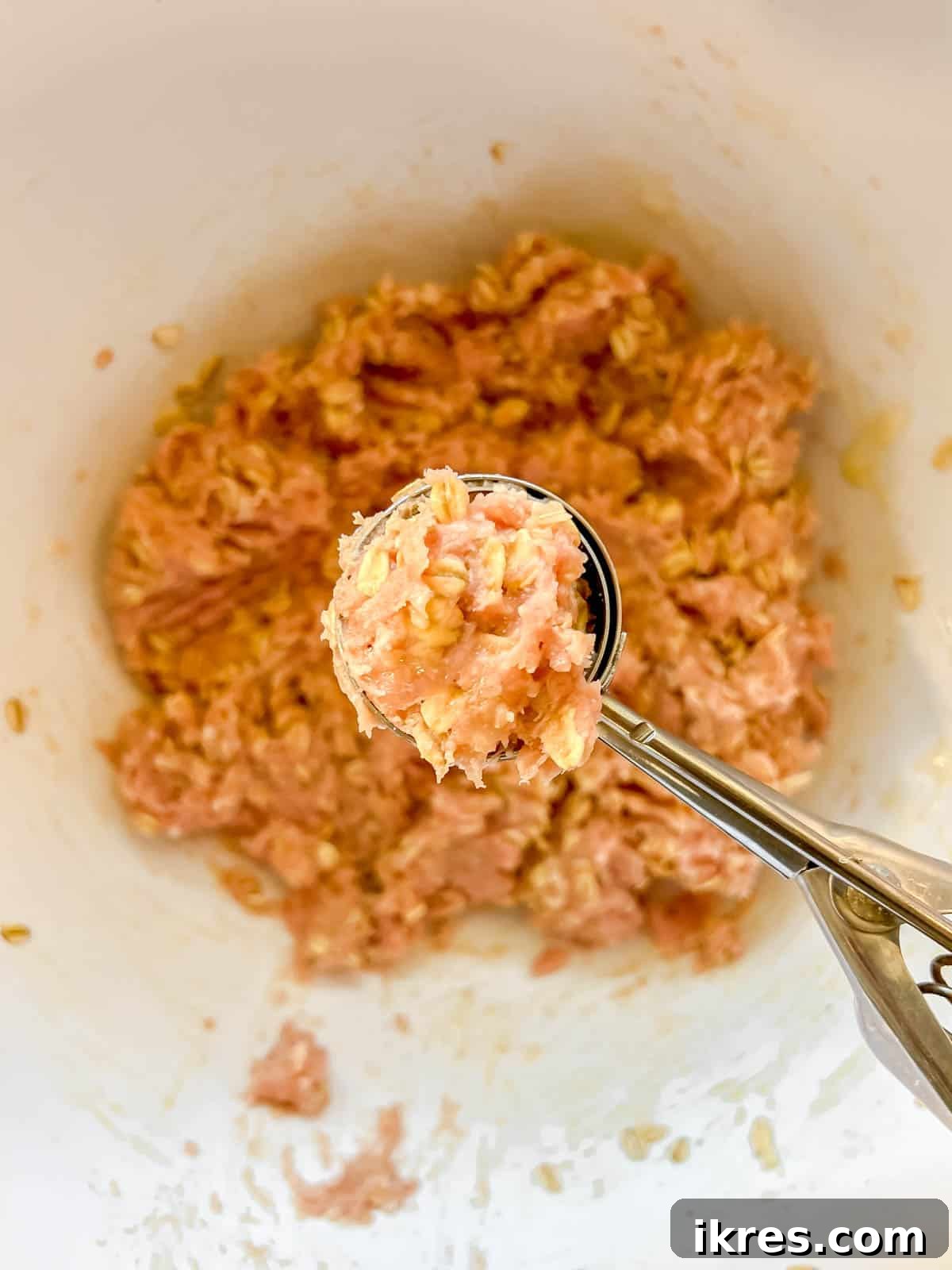A hand scooping and rolling the turkey meatball mixture into uniform balls.