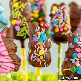 Several chocolate-covered Peeps pops, adorned with sprinkles and standing upright, presented as a festive Easter treat.