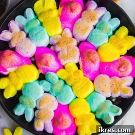 A vibrant Peeps S’mores Dip baked in a skillet, featuring melted chocolate topped with colorful marshmallow Peeps, ready for dipping with graham crackers.