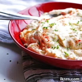Baked mashed potatoes in a red bowl with a spoon, garnished with fresh chives.