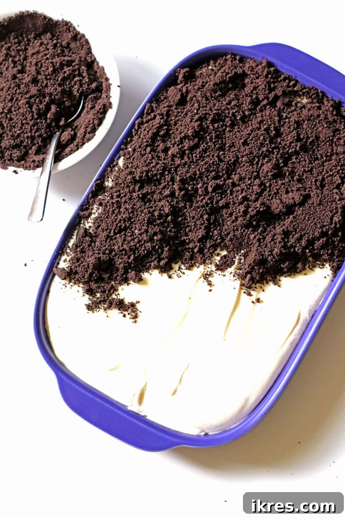 Festive Dirt Cake for Halloween and Easter 5 Finely crushed chocolate cookie crumbs being sprinkled generously over the smooth pudding mixture, creating the 'dirt' layer of the Dirt Cake.