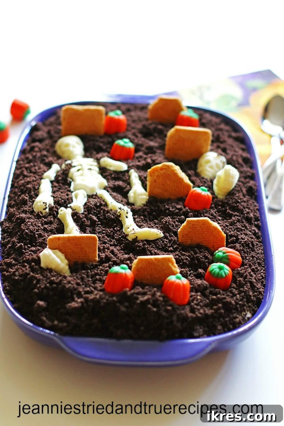 Festive Dirt Cake for Halloween and Easter 6 A Halloween-themed Dirt Cake artfully arranged in a baking dish, depicting a spooky graveyard scene. The 'dirt' is made from crushed Oreos, with cookie tombstones and cheerful candy pumpkins adding to the festive atmosphere.