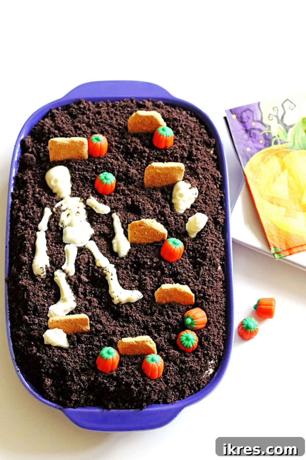 Festive Dirt Cake for Halloween and Easter 10 A fully decorated Halloween Dirt Cake, resembling a festive graveyard. It features vibrant candy pumpkins, a white chocolate skeleton, and artistically modified cookies serving as tombstones, all set against a base of crushed 'dirt'.