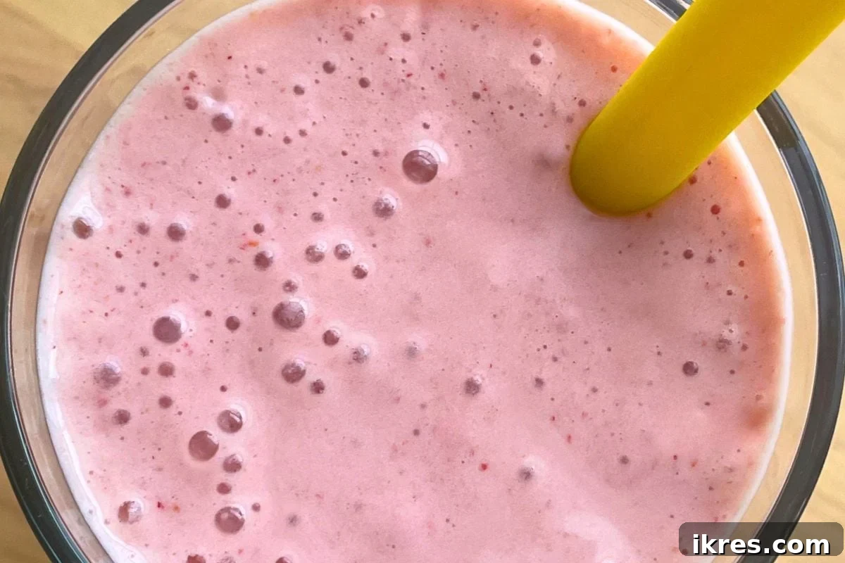 A close-up of a strawberry banana smoothie with a yellow straw with bubbles on top.