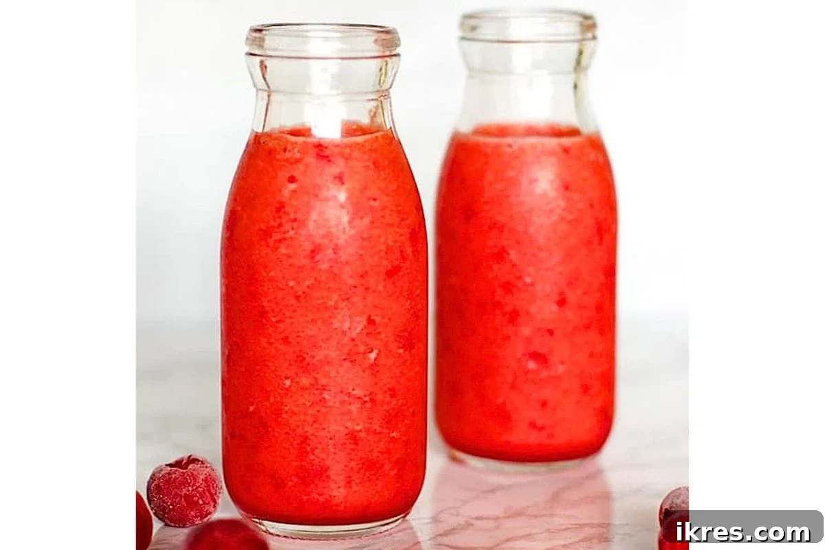 A red cherry pineapple smoothie in a glass with a straw.