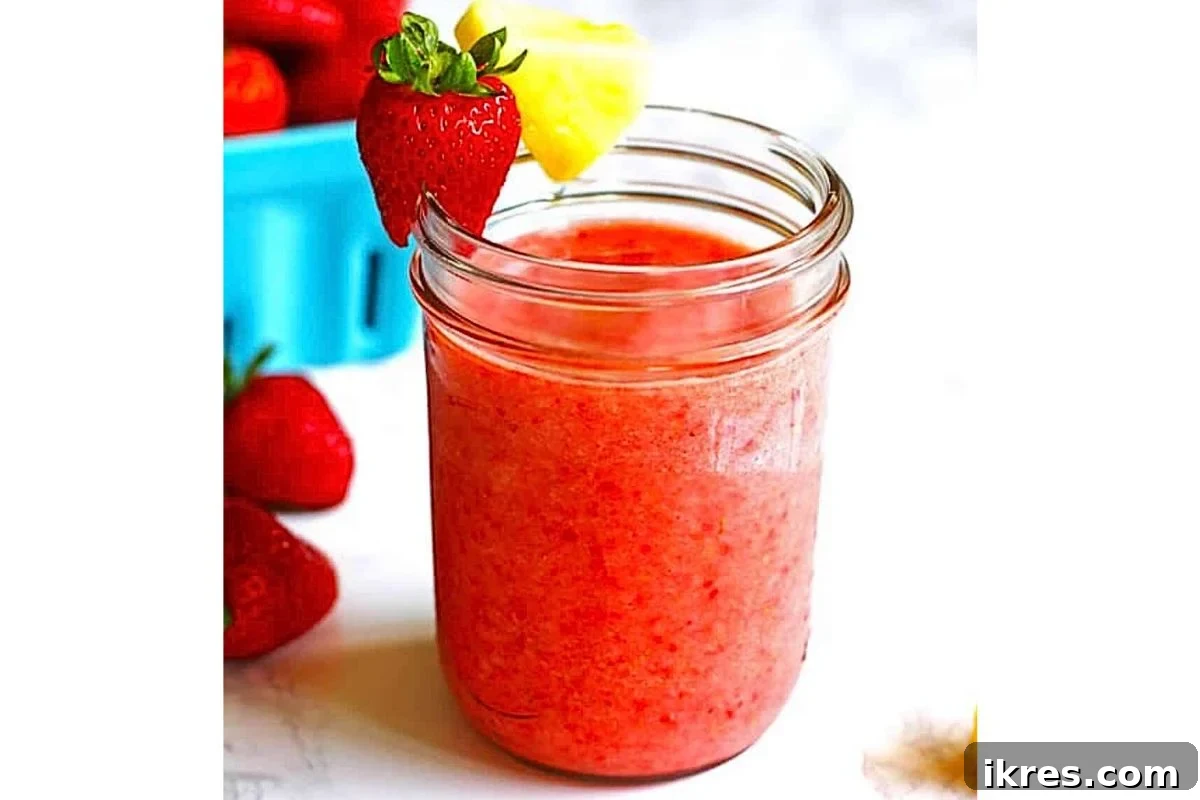 A glass of strawberry pineapple smoothie with a straw and a slice of pineapple.