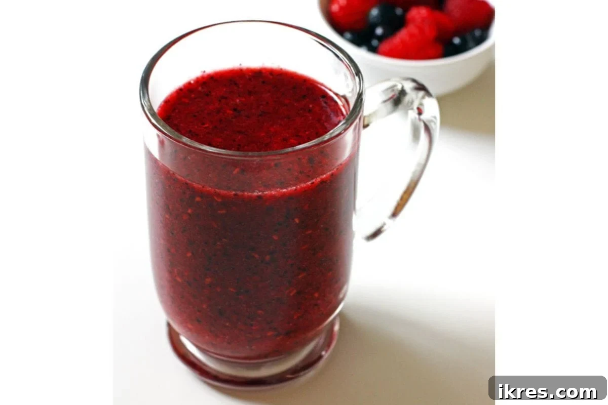 A glass of triple berry smoothie with a straw, garnished with fresh berries.