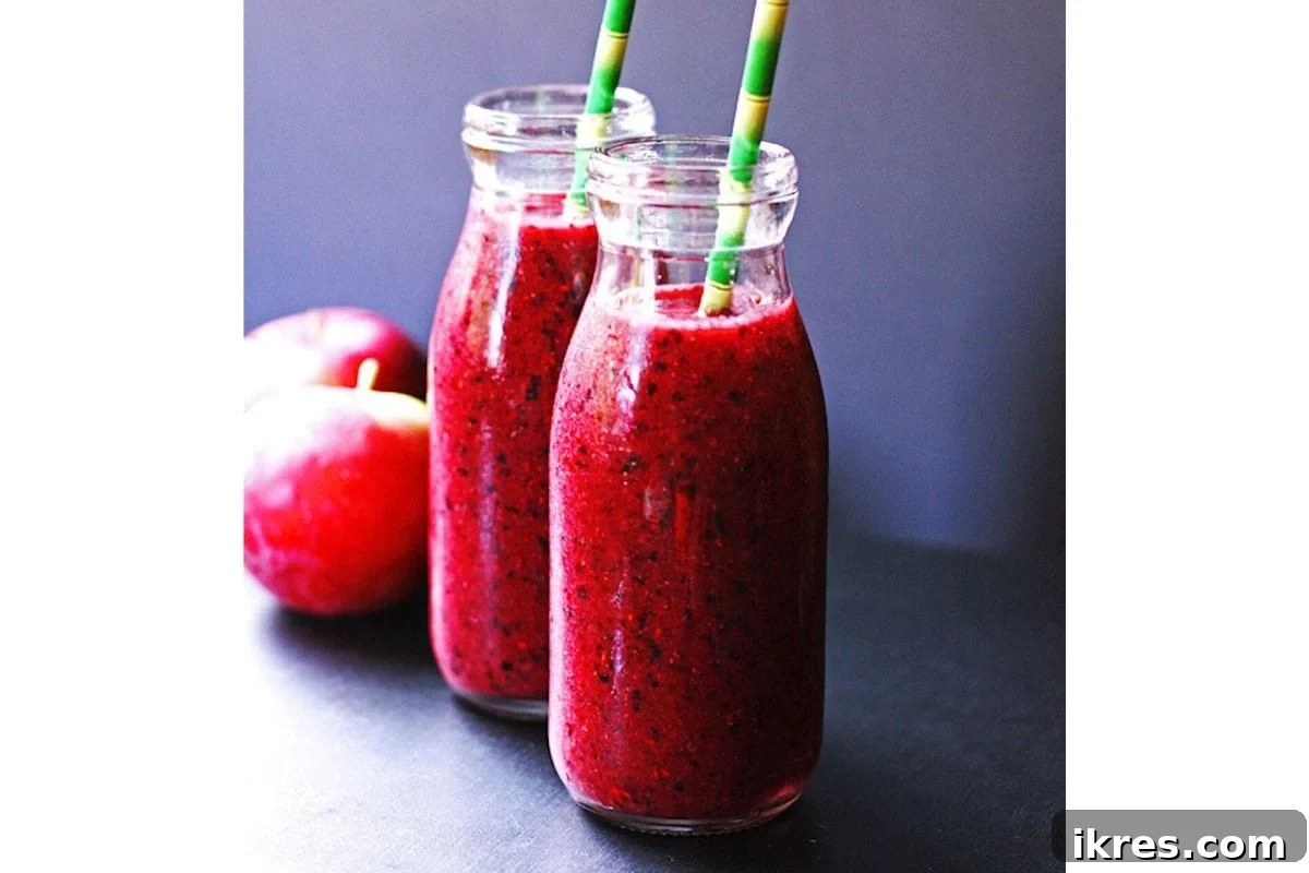 A glass of apple berry smoothie with a straw, garnished with fresh berries and an apple slice.