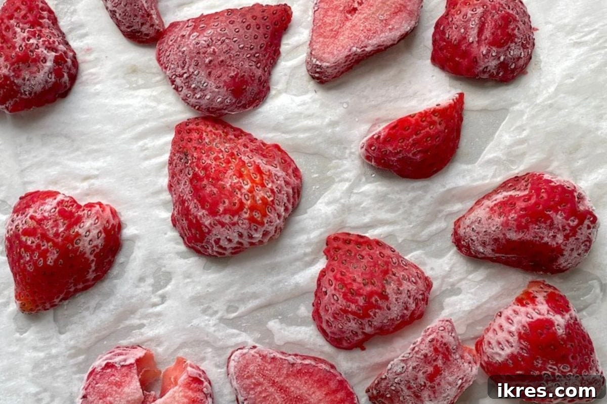 Strawberries spread in a single layer on a baking sheet for freezing.