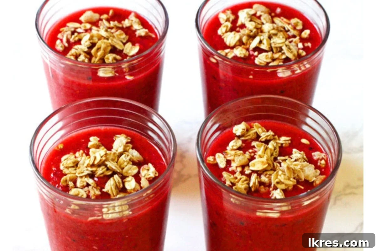 A glass of a berry granola smoothie with a spoon in it.