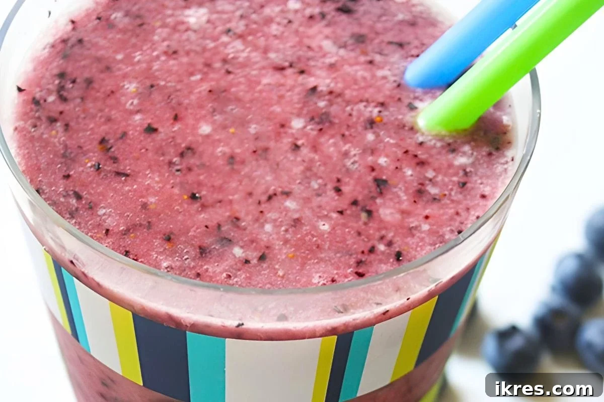 A glass of blueberry banana peanut butter smoothie with a straw and blueberries on top.