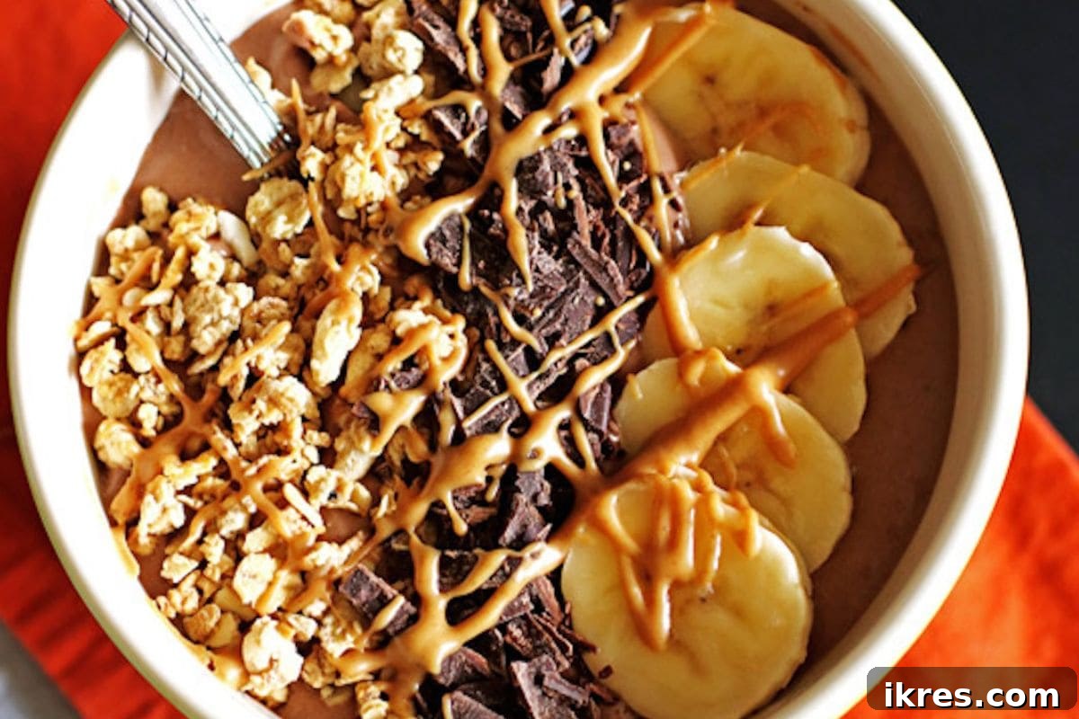 A chocolate peanut butter smoothie bowl topped with sliced banana, chocolate chips, and chopped peanuts.