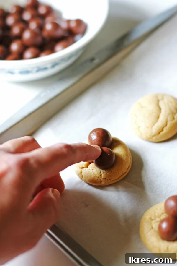 The step of gently pressing Whopper candies onto warm peanut butter cookies to form the base of the candy spiders.