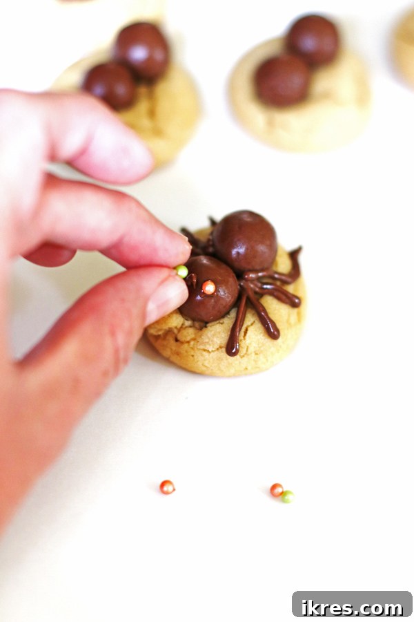 The final step of decorating: carefully placing colorful candy sprinkles onto melted chocolate dots to create the spider's eyes on top of the cookies.