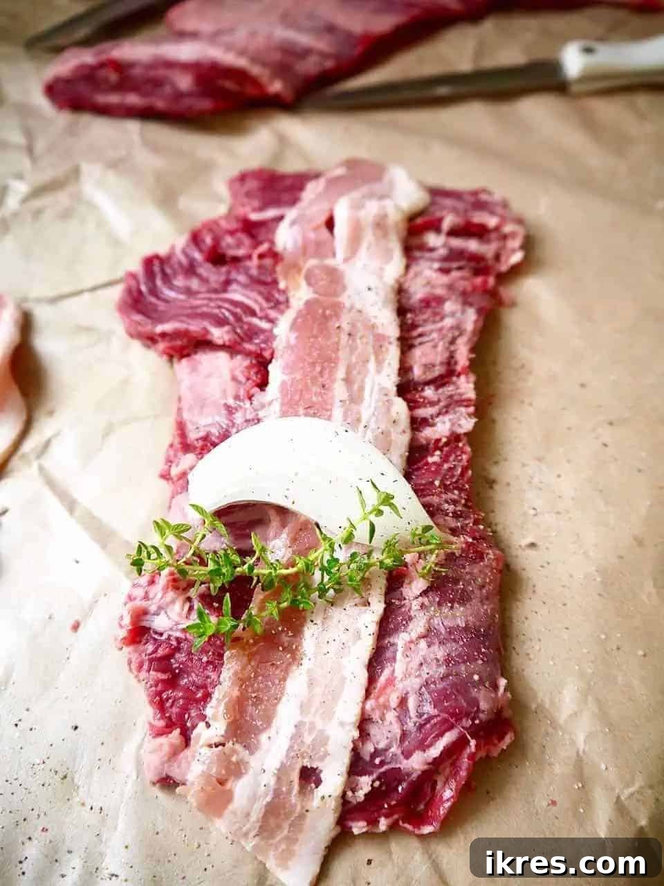 Beef Roulade Stuffed with Smoky Bacon, Sweet Onion, and Fresh Thyme 4 Thinly sliced beef steak laid flat with a piece of bacon and onion wedge on top, ready for seasoning.