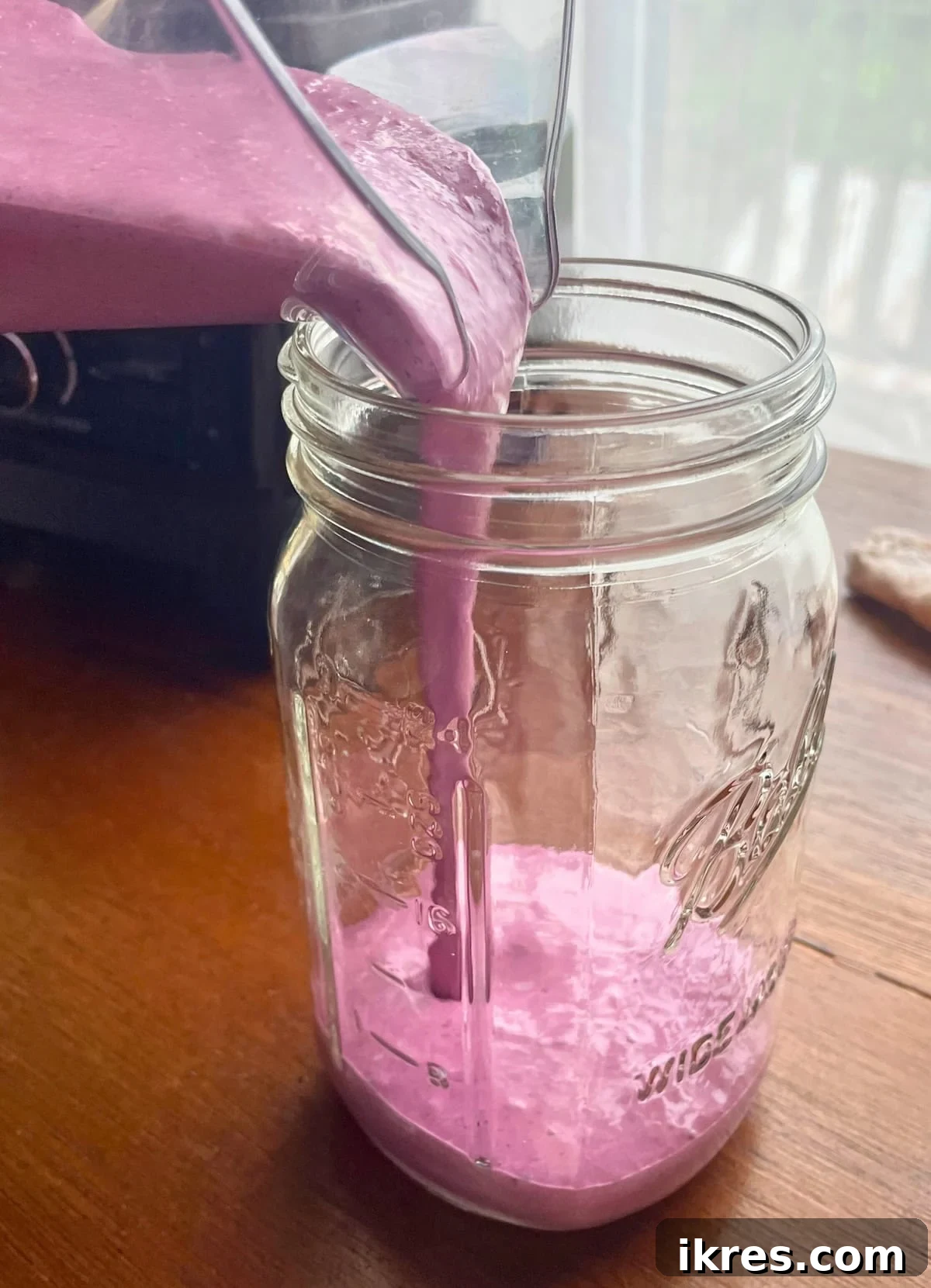 Vibrant Blueberry Pineapple Blast 6 A rich, purple blueberry pineapple smoothie being poured from a high-speed blender into a large glass mason jar, highlighting its creamy texture.