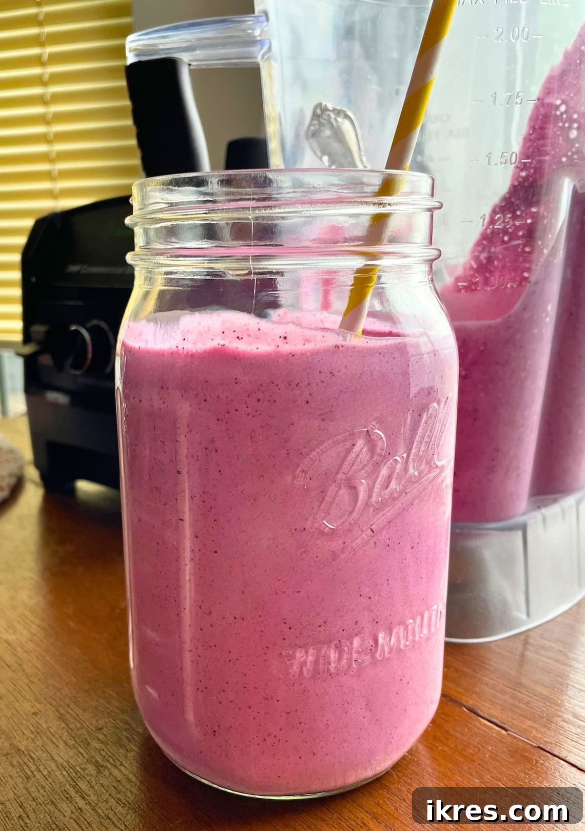 Vibrant Blueberry Pineapple Blast 7 A generously sized blueberry pineapple smoothie in a large mason jar with a bright yellow straw, set against a blurred outdoor background, emphasizing its refreshing appeal.