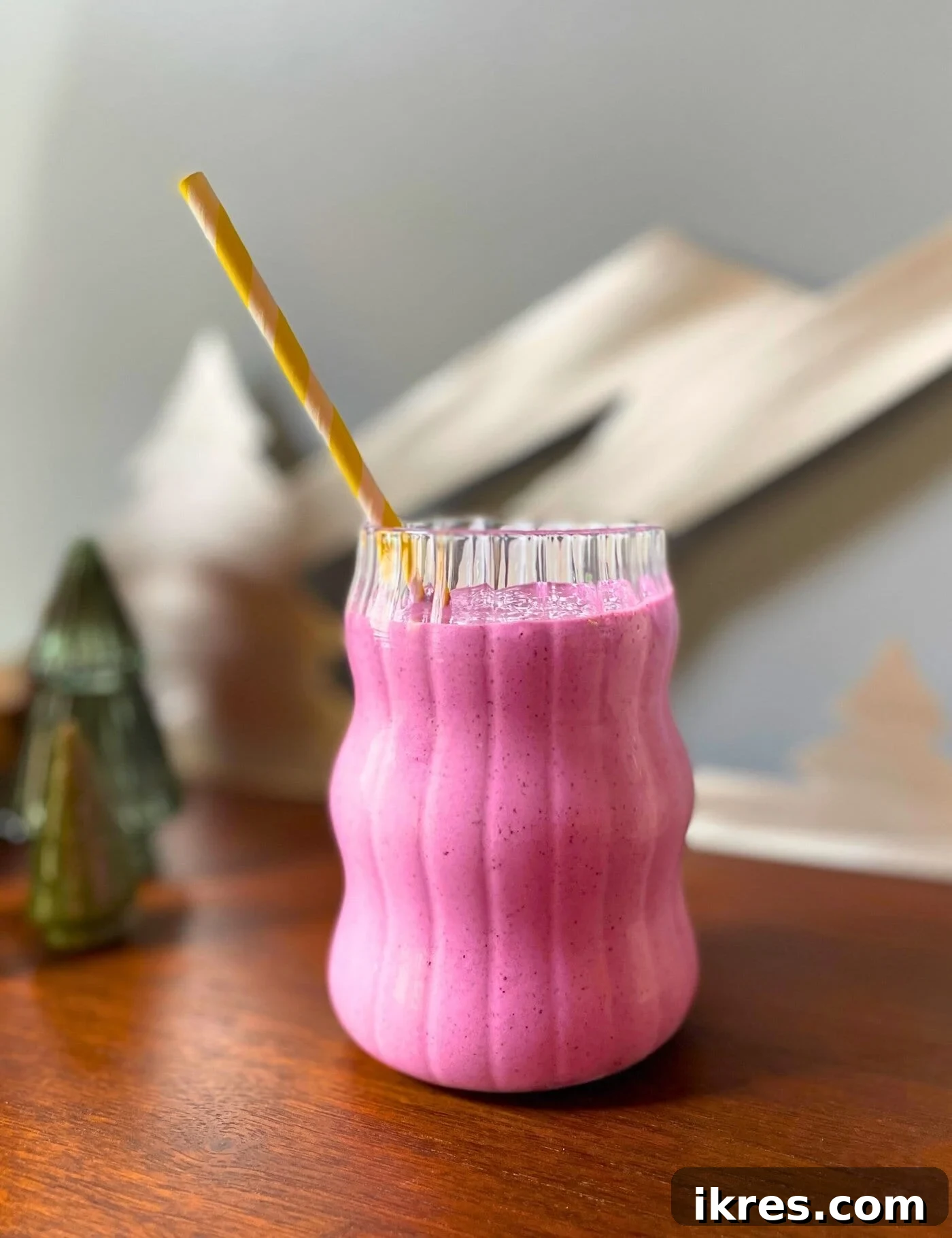 Vibrant Blueberry Pineapple Blast 8 A vibrant pineapple blueberry smoothie with a yellow straw, placed on a wooden cabinet next to a rustic mountain sign and decorative glass trees, creating a cozy indoor scene.