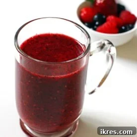 A mug of Triple Berry Smoothie with a bowl of mixed berries behind it.