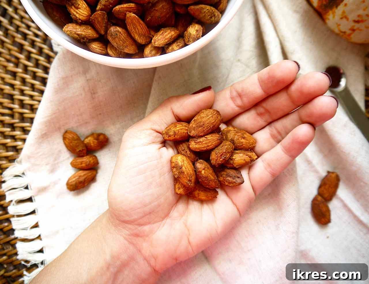 A hand holding a small pile of freshly roasted pumpkin spiced almonds, highlighting their crunchy texture and even coating.