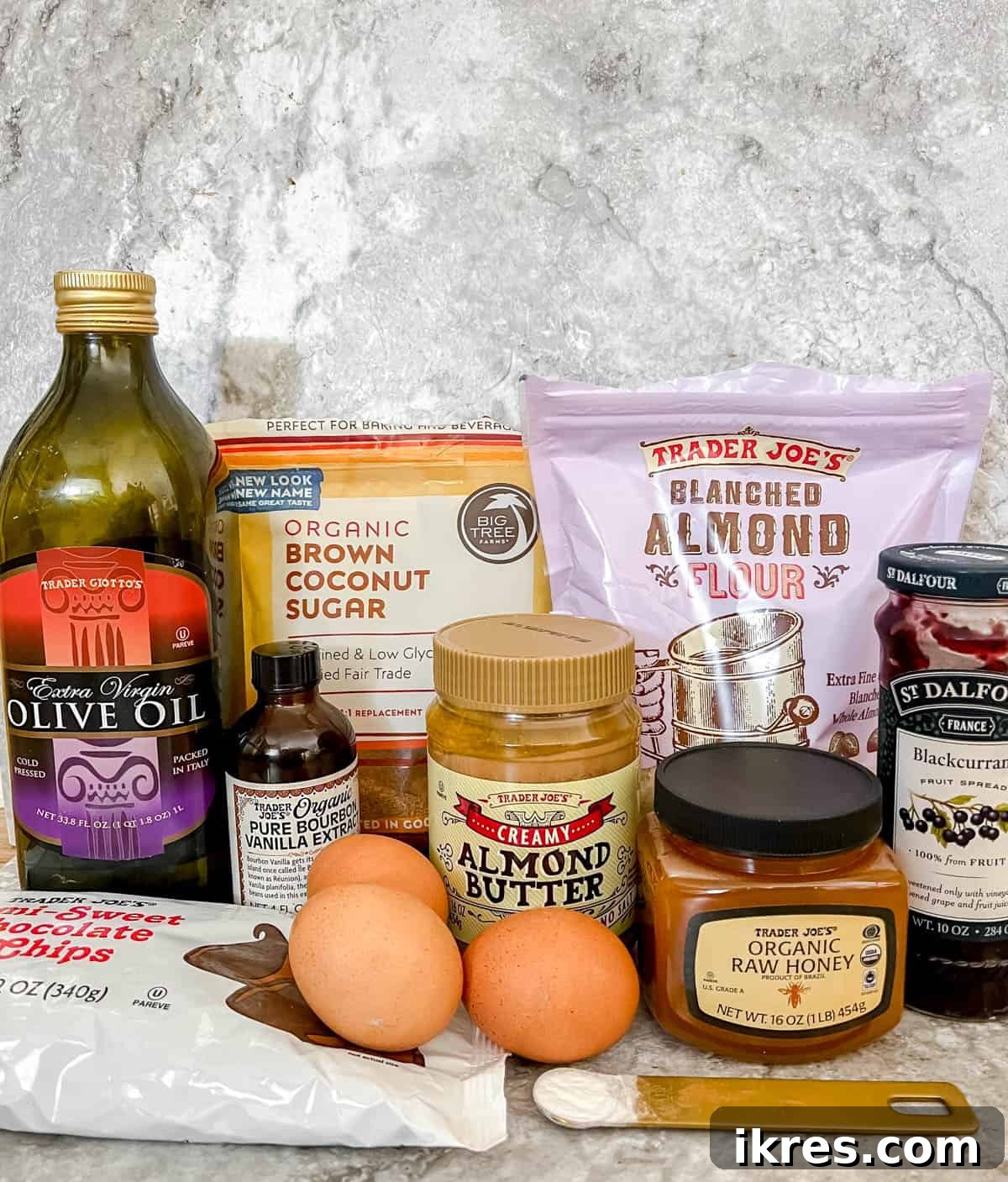 Ingredients needed to make delicious almond butter and jelly brownies: olive oil, chocolate chips, coconut sugar, eggs, almond flour, baking soda, honey, almond butter, and berry jam.