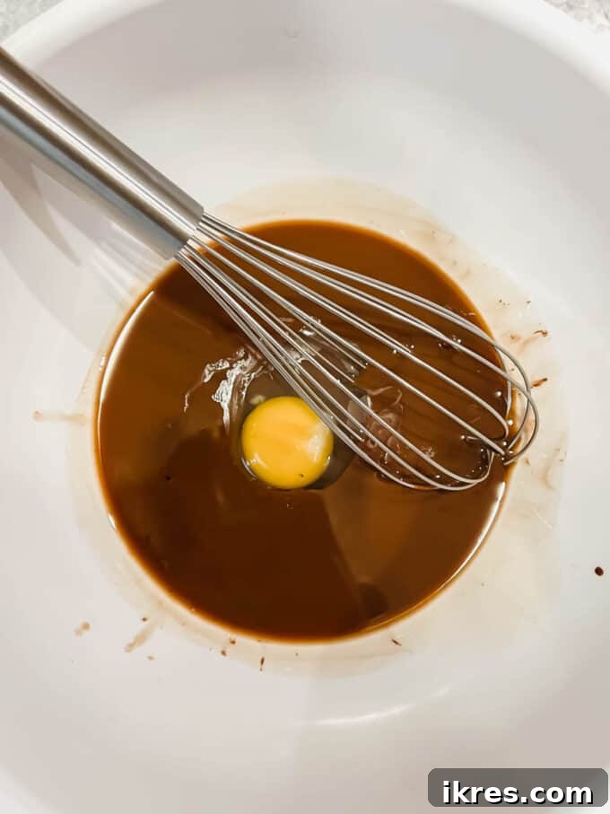 Whisking eggs one by one into the chocolate mixture for a fudgy brownie texture.