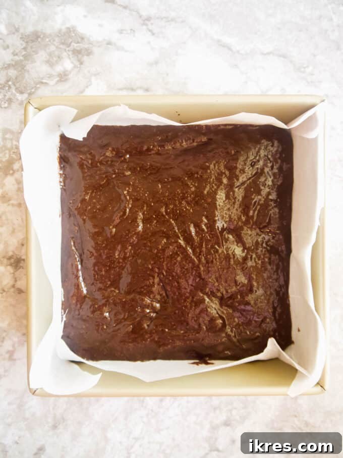 Brownie batter evenly poured into a parchment-lined baking pan.